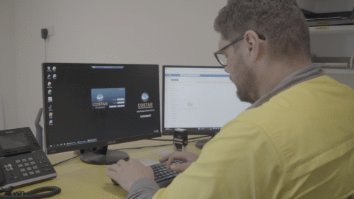man seated at a desk working on a computer with dual screens